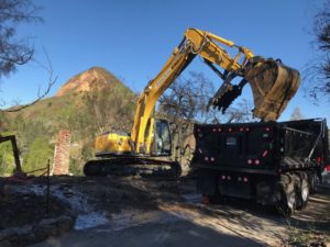 State contractors use an excavator to help remove debris caused by the Woolsey Fire from a property in the Seminole Springs Mobile Home Park earlier this year