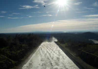 A skycrane helicopter carries a load of rock above the flowing Oroville Dam Spillway