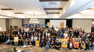 Group photo of Listos conference attendees, taken on a stage in a hotel ballroom. Some attendees holding Listos California posters.
