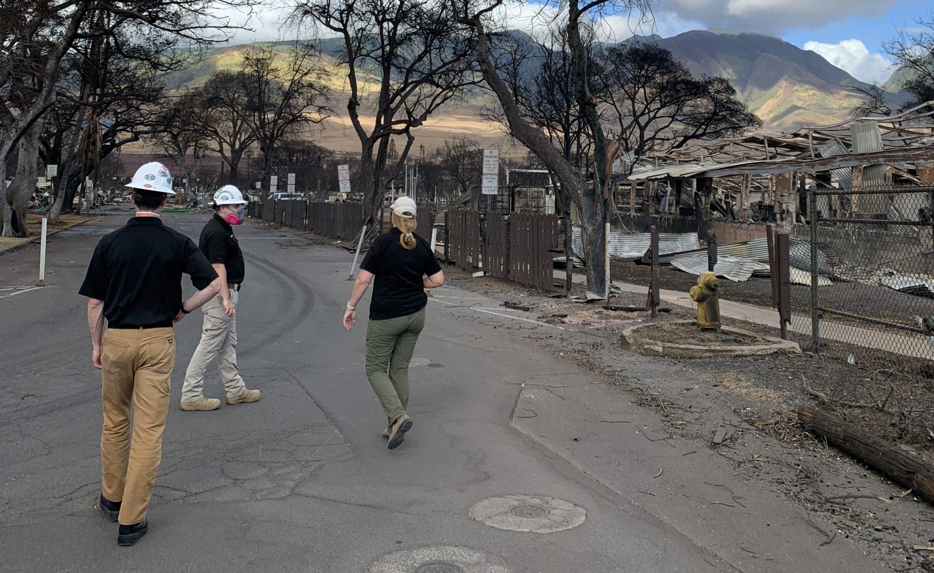A photo of Cal O E S debris removal team in Lahaina, Hawaii. They're inspecting the burnt debris and wearing personal protective equipment. 