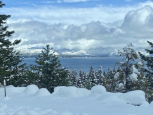 A photo of snow covered hills with Lake Tahoe in the background. Pine trees line the left and right of the image.