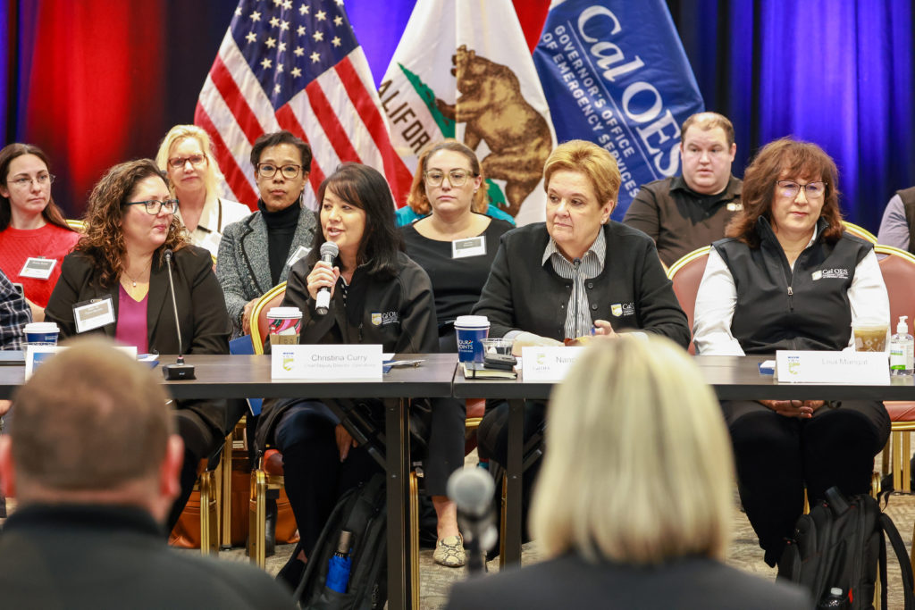 image of people sitting at a table. American, state and cal O E S flags in background.