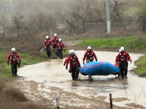 responders wade through a full river carrying a life-saving raft