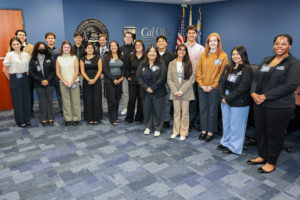 A group of women and men stand in front of a wall that has the seal of California and the Cal OES logo on it.