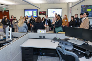 A group of people listen as two women standing before them talk.