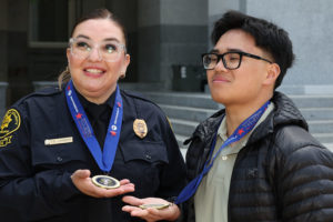 Emergency dispatcher Lucia Guzman and her 911 caller hero Aaron Nguyen, stand together holding their medals.