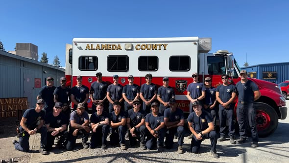 a group of firefighters pose in front of a Alameda County fire truck.