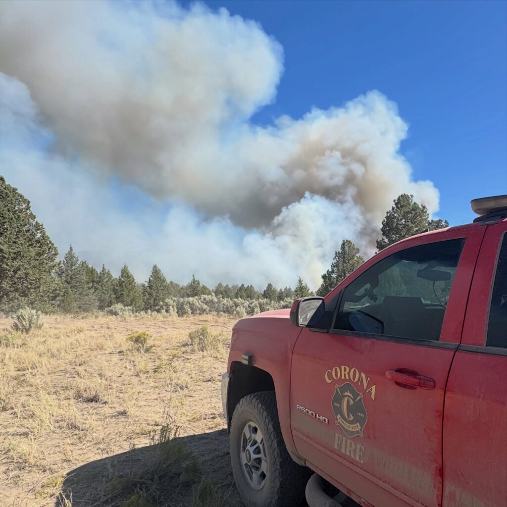 A red fire truck in the foreground faces an open field and smoke in the background.