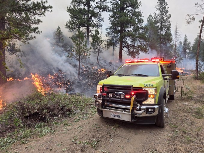 A Cal OES fire engine on a dirt road near flames