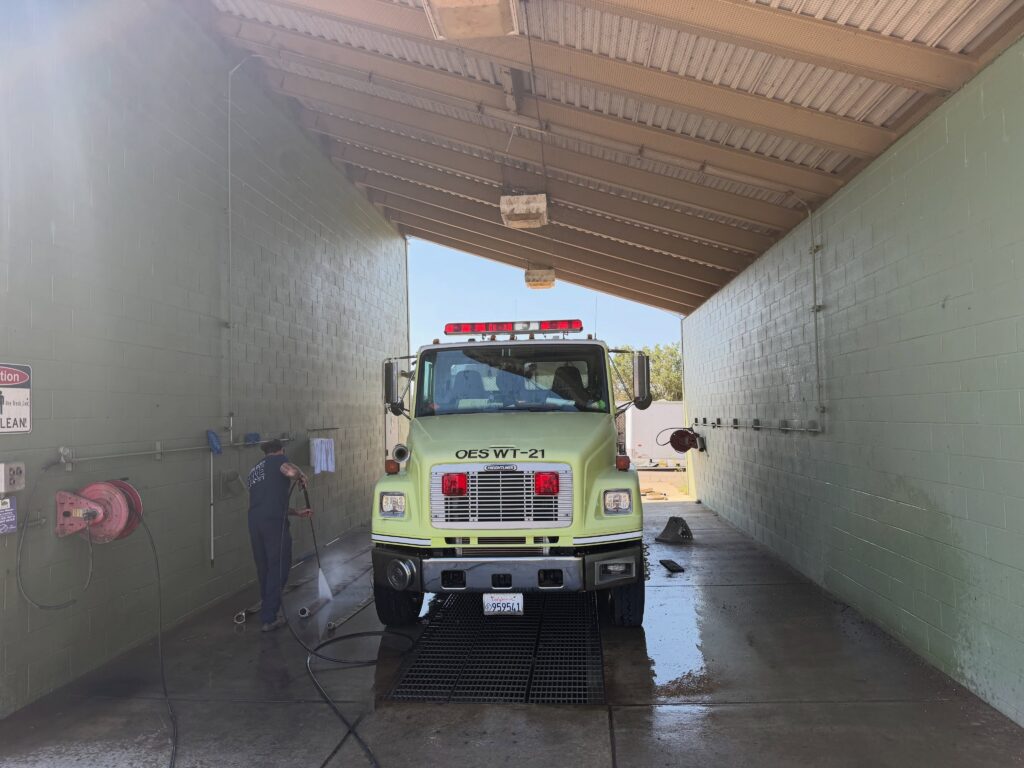 a firefighter washes a yellow fire truck in a bay.