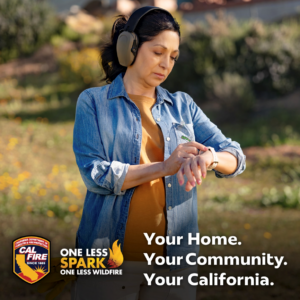 A woman standing outside in a field wearing headphones, checks her watch.
