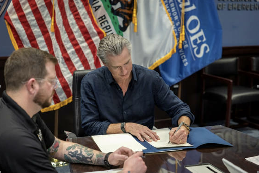governor Gavin Newsom sitting at table signing emergency proclamation